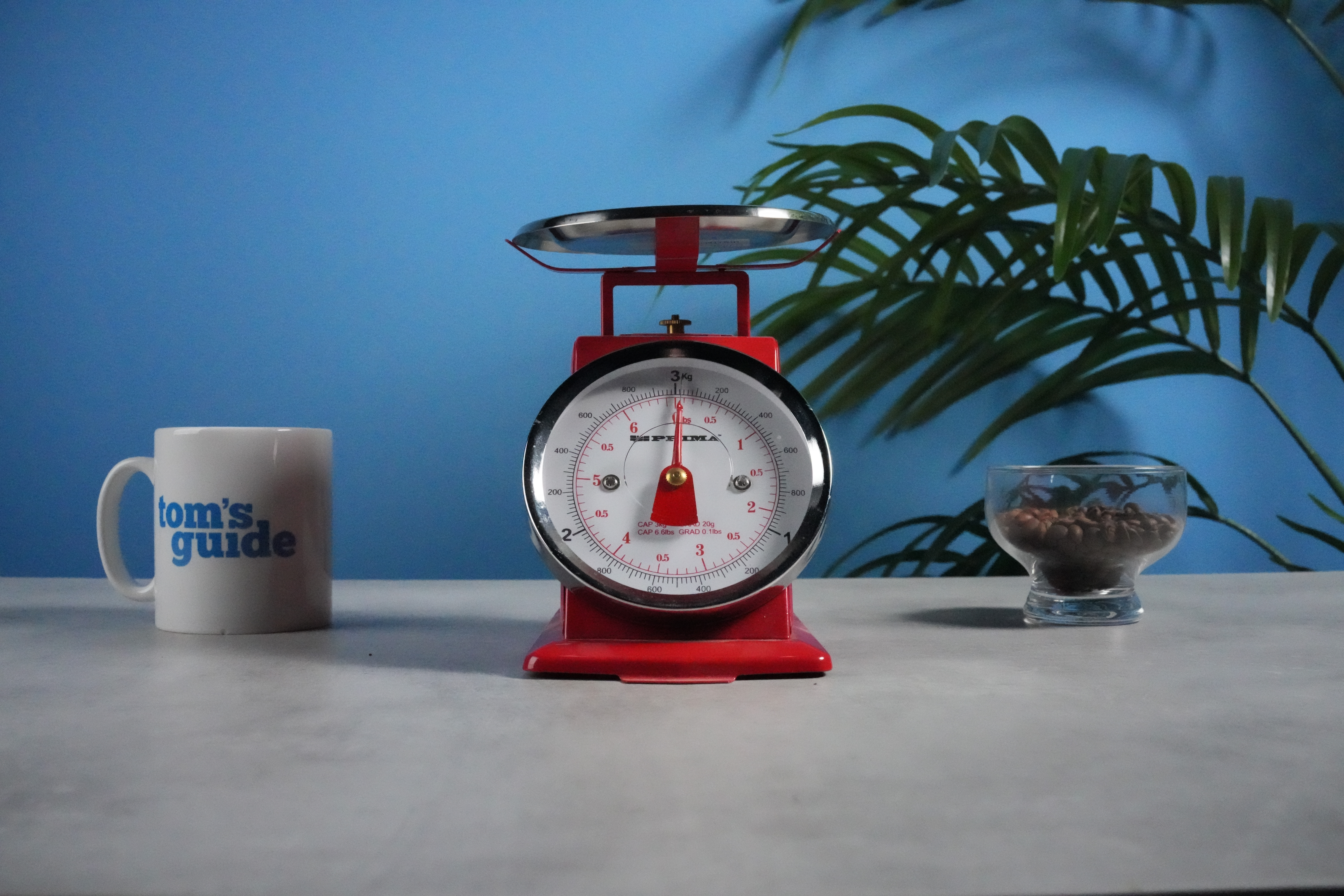 A photo of a set of red scales next to a Tom's Guide mug and some coffee beans, with a blue wall in the background