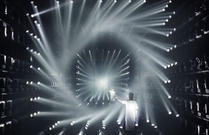 Inside a room filled with lights forming light beams and two people standing with their hands to the side. 