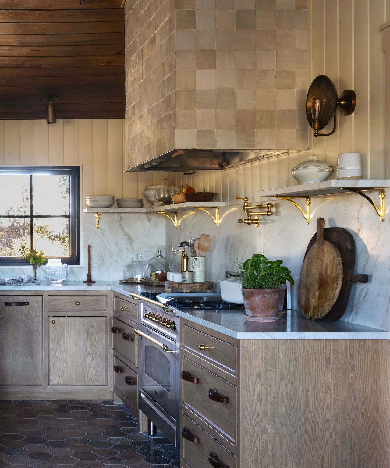 A warm, rustic kitchen with wooden cabinets a marble backsplash and textured square tiles covering the stove's hob