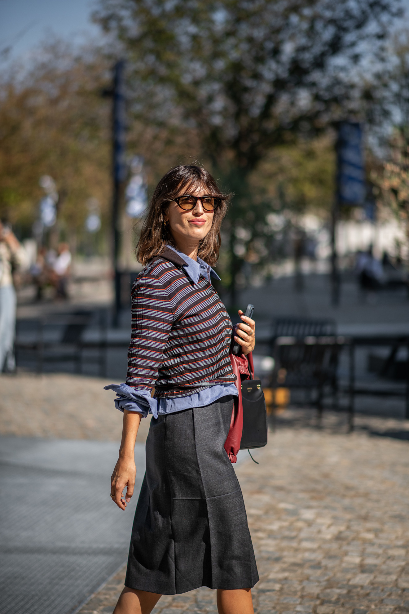 a white woman with a brunette lob in a striped sweater and midi skirt