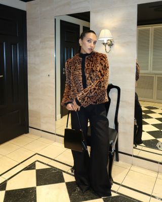 Ingrid wears a leopard fur coat, black pants, and a black bag.