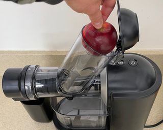 Helen McCue placing a whole red apple into the chute of the Philips Viva Masticating Juicer