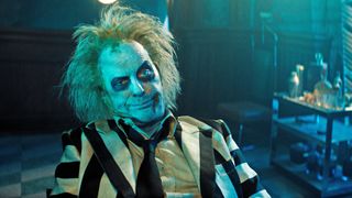 Michael Keaton's Beetlejuice pulls a funny face while sitting down in Beetlejuice Beetlejuice