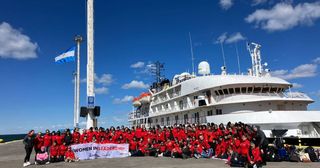 All passengers wearing matching red jumpsuits in front of the ship that will take them to Antarctica.
