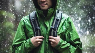 A man hiking in the rain wearing a green waterproof jacket