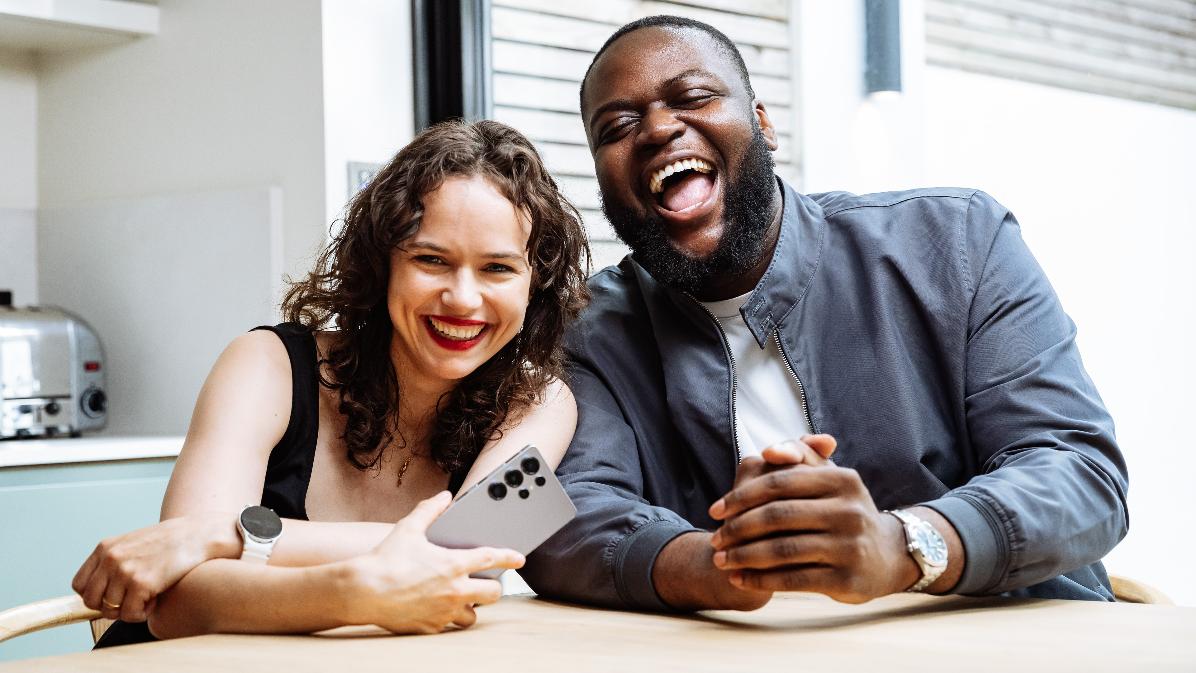 Two people laugh sat down holding Samsung phone