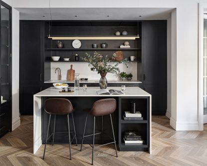 A white island with dark cabinets and brown leather bar stools