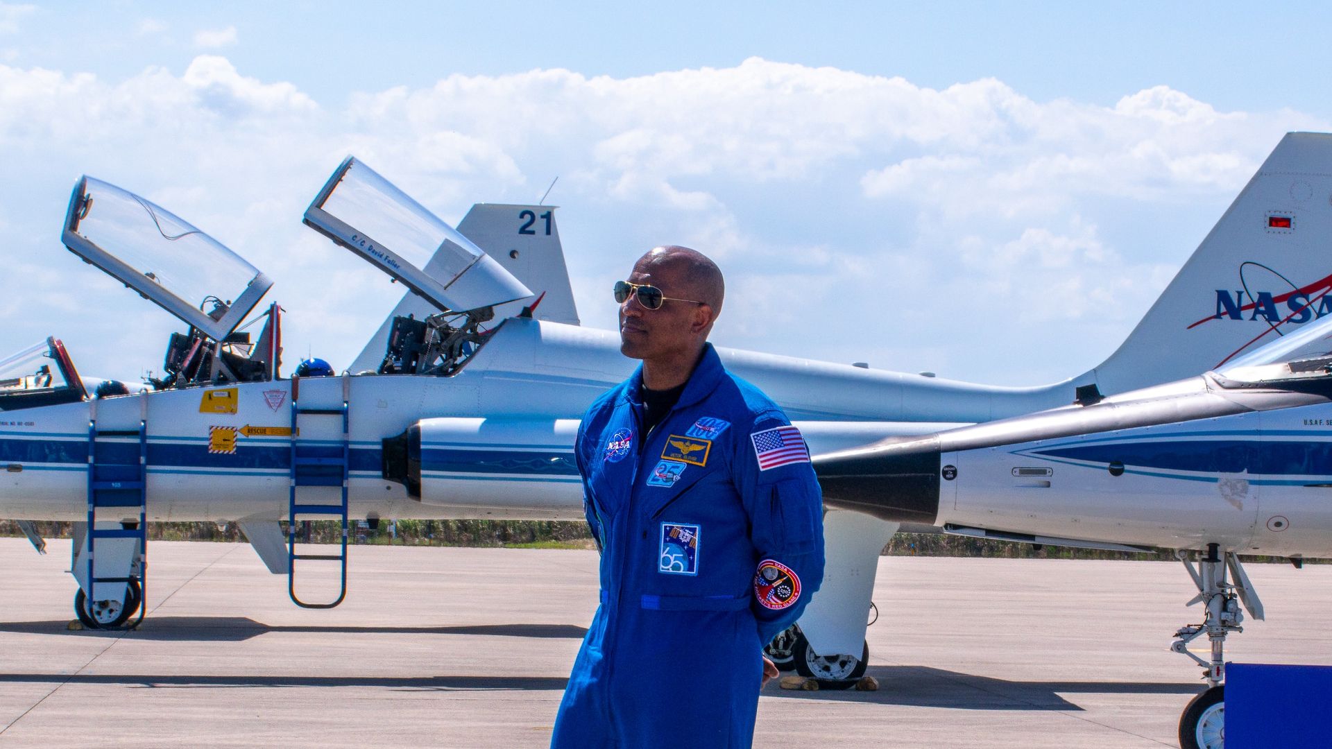 A man in a blue jumpsuit stands in front of giant a trio of NASA jets.