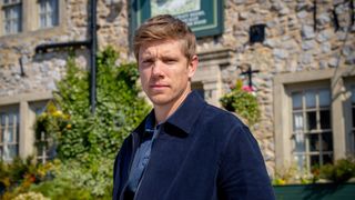 Robert Sugden standing in front of The Woolpack. He is wearing a blue jacket and shirt.