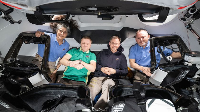 Three men and a woman in polo shirts and a hoodie float inside a spacecraft for a photo together