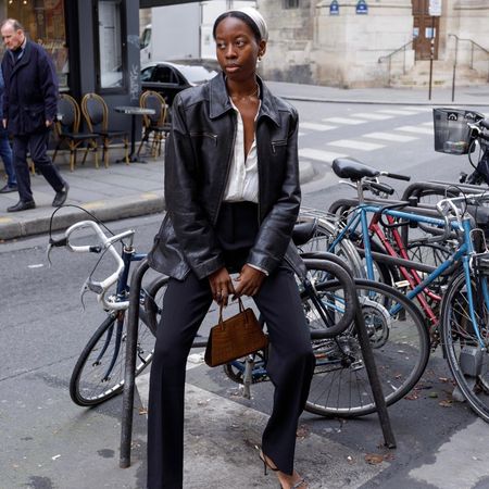 French fashion influencer Syvlie Mus is Paris wearing an on-trend fall look including a vintage leather jacket, head scarf, white shirt, black pants, strappy heels, and a mock croc bag.