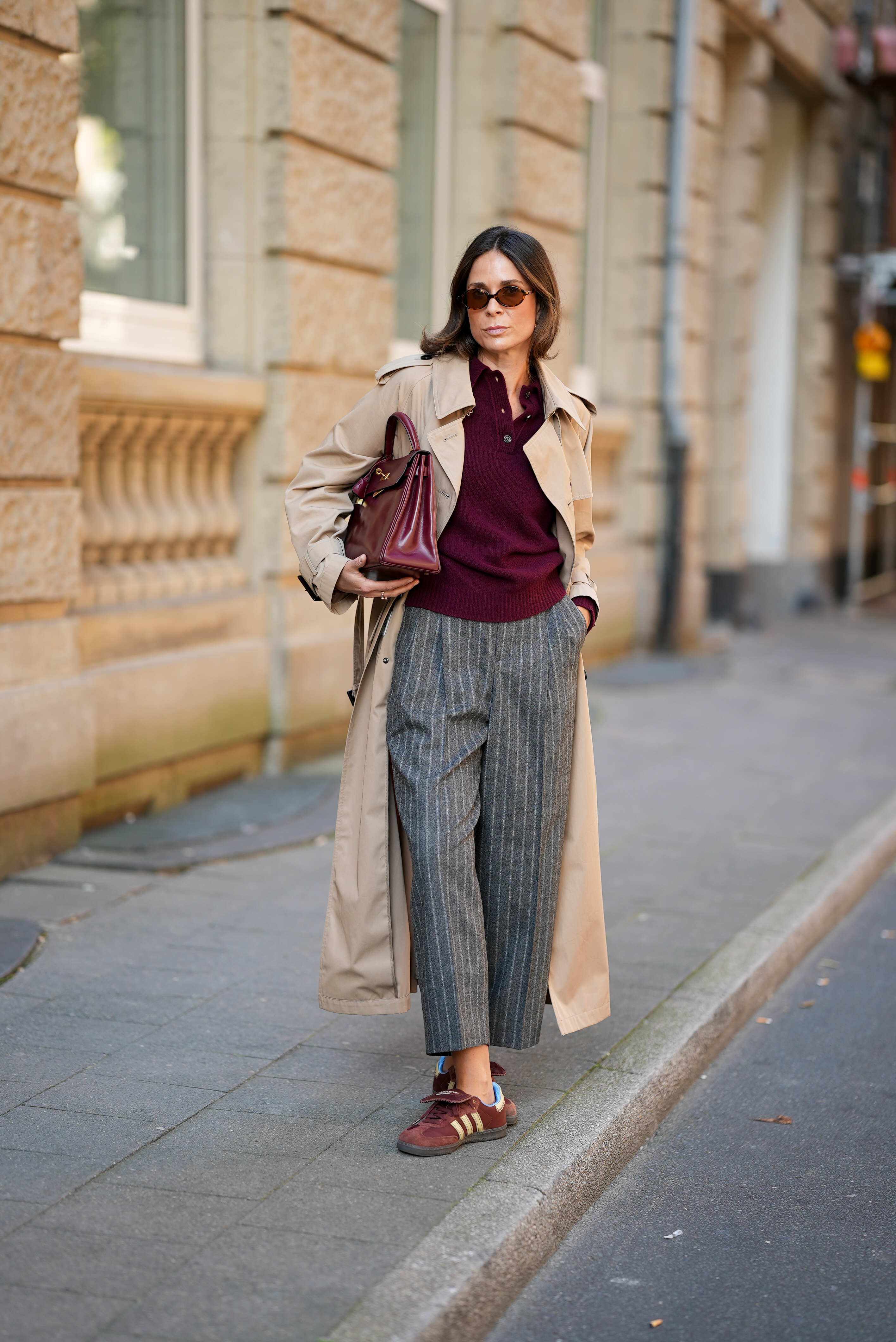 Woman in gray trousers, a trench coat, and a red polo sweater.