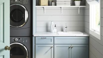 sterling sink in small laundry room with blue cabinets, white worktop, stacked washing machine and dryer
