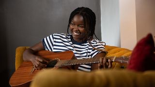 Teenage girl smiling while she plays acoustic guitar on an orange couch