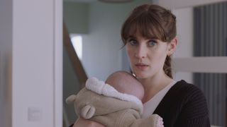 Anna Chell as Jodie Whyte, holding a baby in a warm onesie while she looks wide eyed and worried.