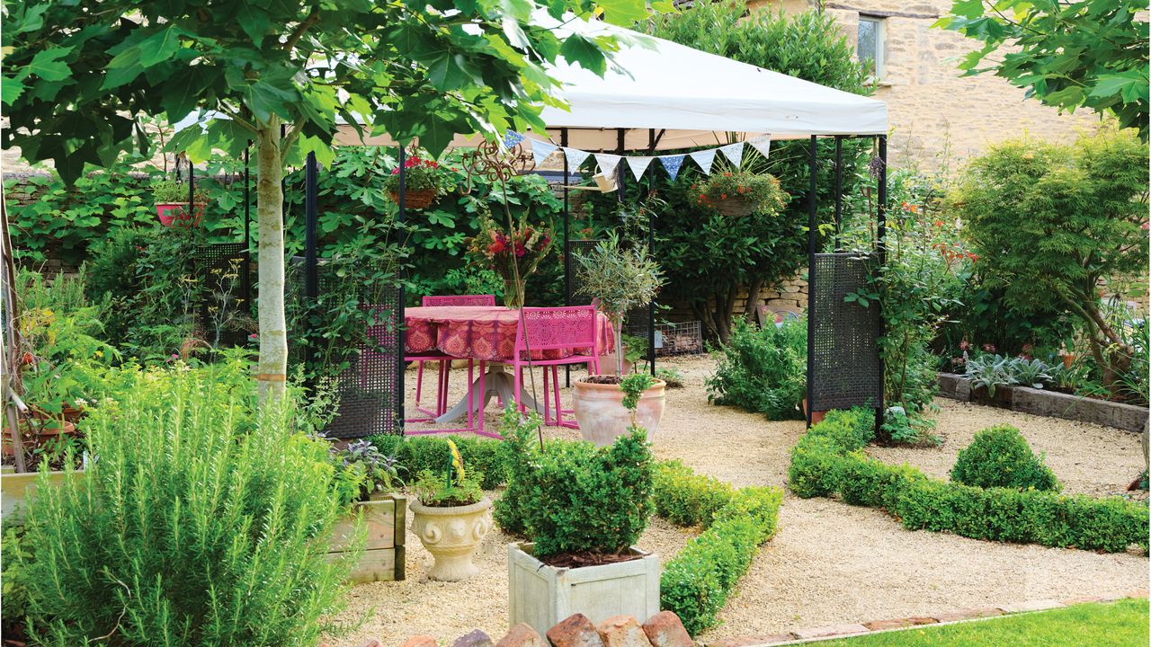 garden with white pergola, pink dining table and chairs, potted plants and green borders