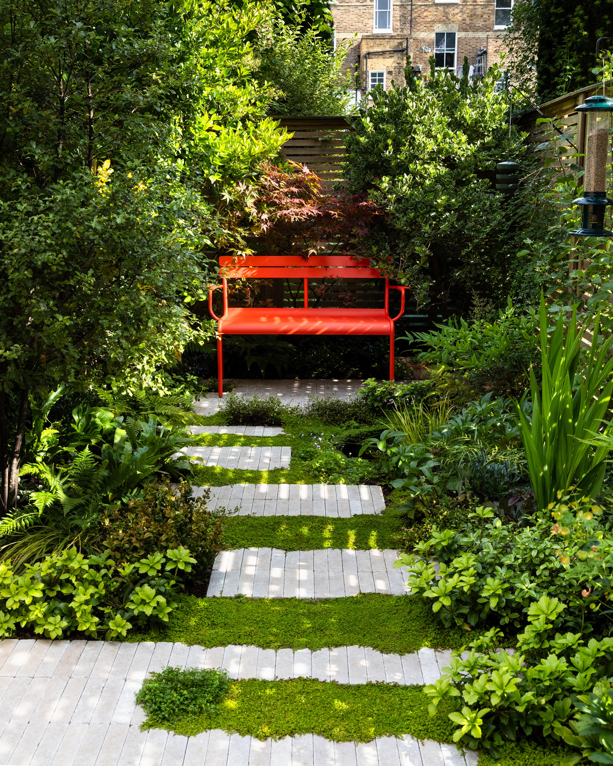 a small london garden with pavers between mind your business and a bright red bench seat