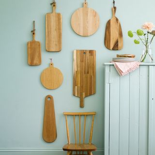 Green wall with a selection of wooden chopping boards hung to create a display