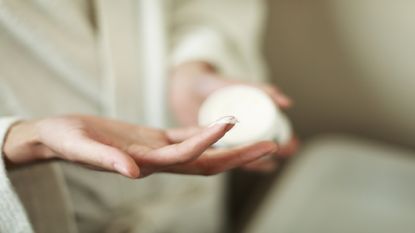 Unidentifiable person using finger to take moisturiser cream out of pot