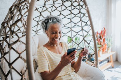 A woman sits outside while smiling at her smartphone. 