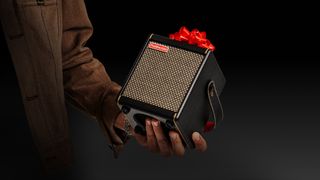 Man holding a black Positive Grid Spark Mini amp with a red bow on top