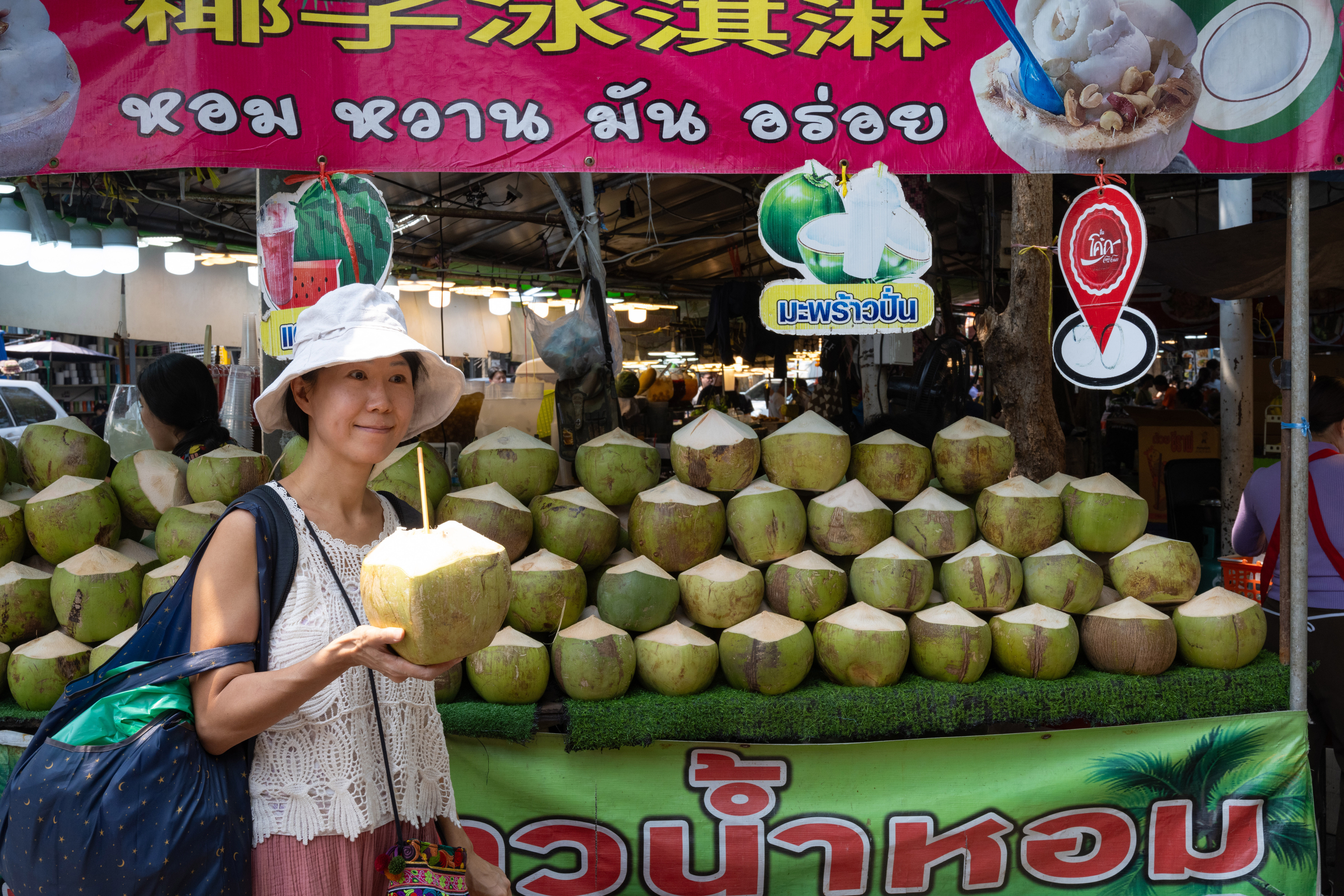 A woman wearing a white hat drinks coconut milk at Chatuchak Market