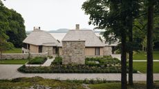 exterior of sustaianable home with sprawling garden, stone walls, timber walls, and view of water