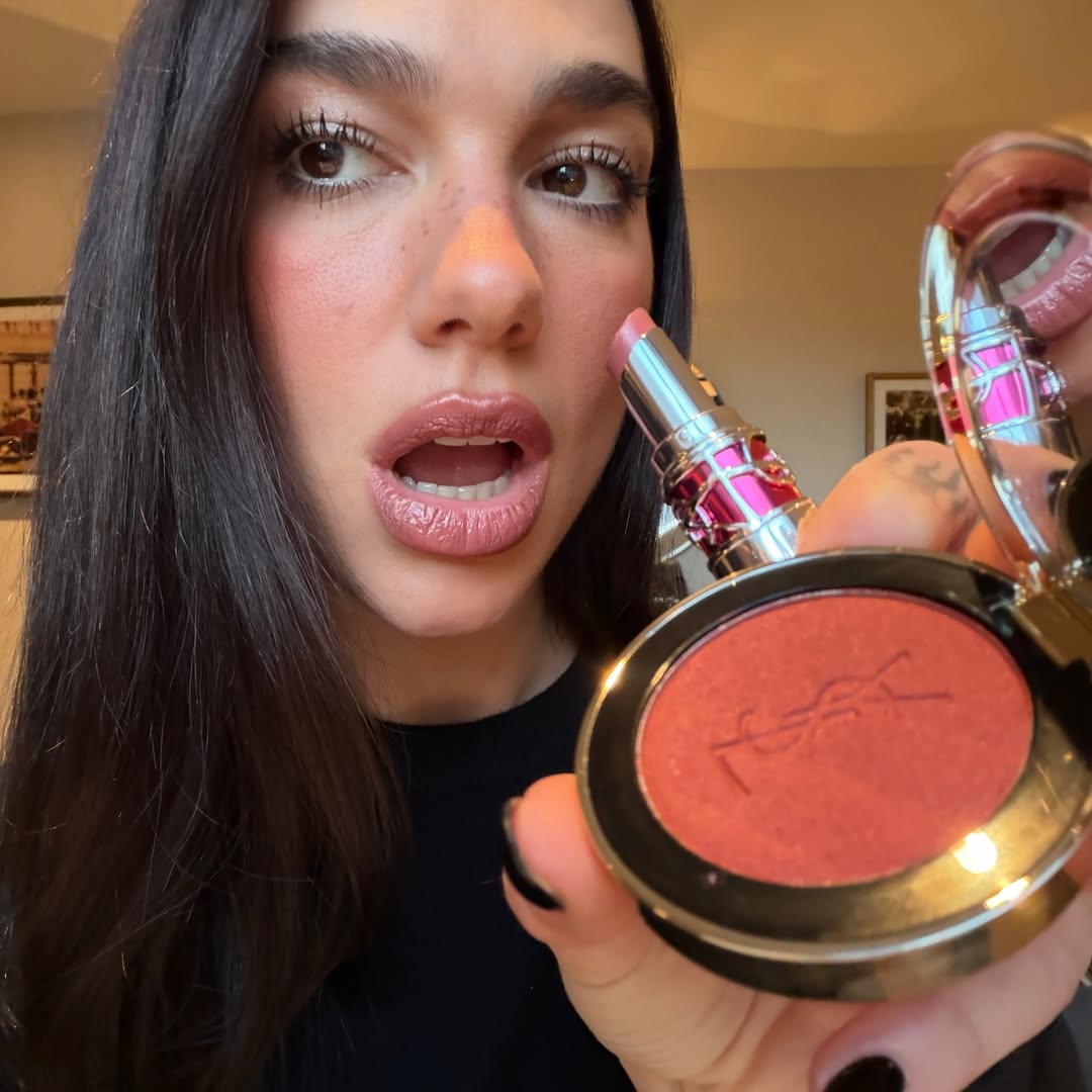 Dua Lipa holding two YSL beauty products.