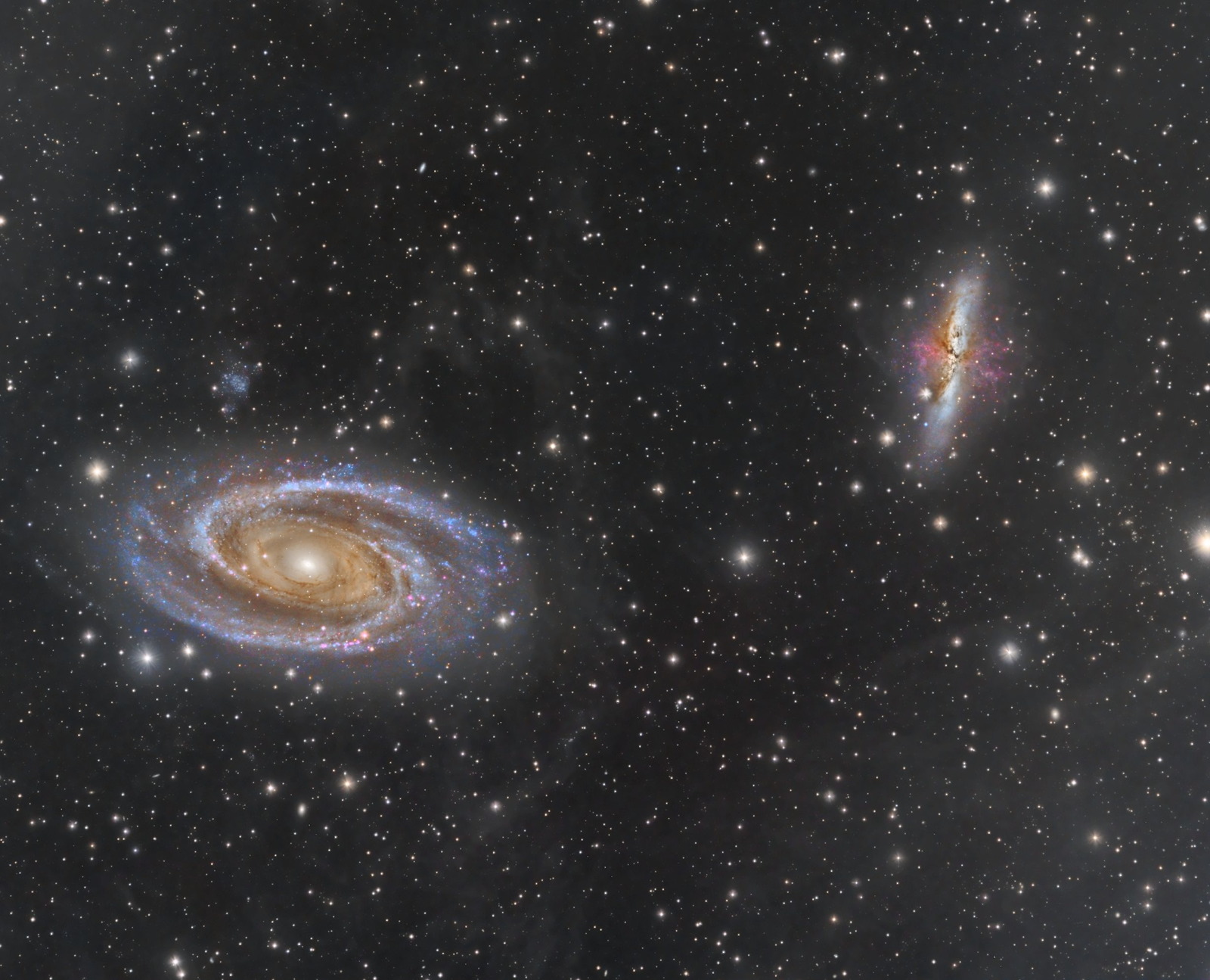 Two galaxies are seen in a starry sky. The one on the left is a spiral and the one on the right has more of an elongated shape.