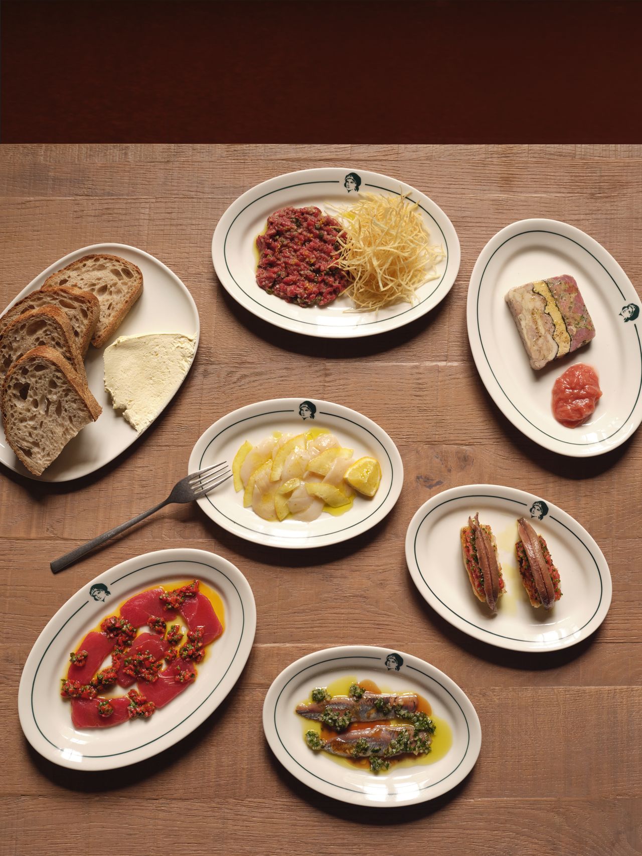 A series of restaurant plates, characterized by colorful, striking presentations, is captured in white dishes against a wooden surface from above.