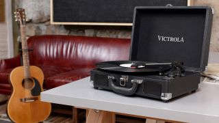 Victrola Journey turntable review: The Victrola Journey turntable atop a table beside a red sofa and acoustic guitar