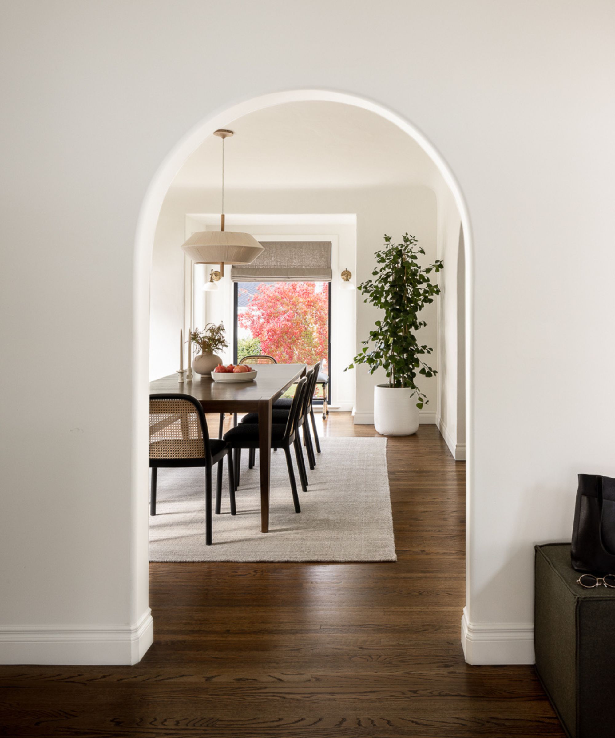 Arched doorway looking into dining room with wooden long table, cane chairs and low pendant light with wood floor