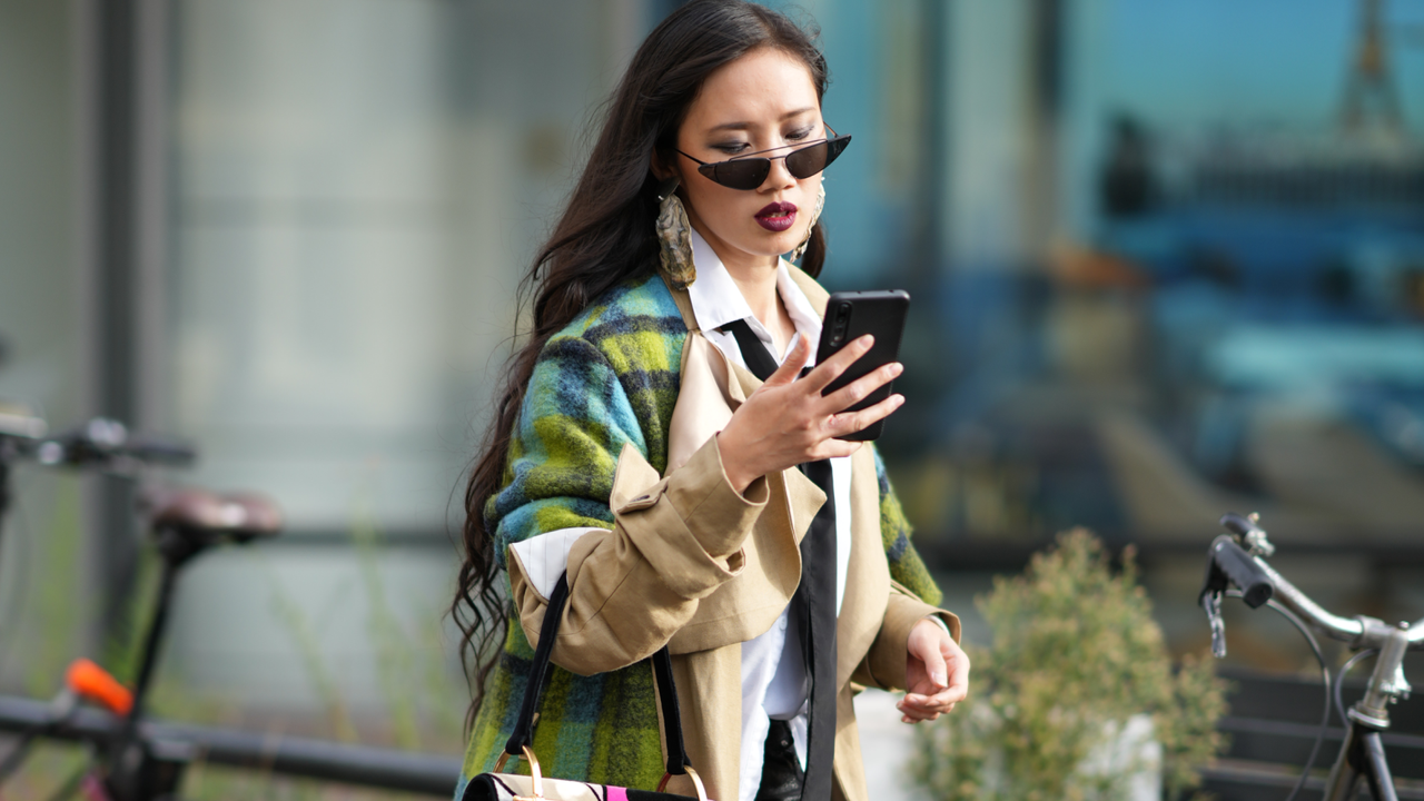 A guest wears sunglasses, a blue and green checked long wool coat, a bag with printed face-design, black leather pants, pointed high heels boots, outside Germanier, during the Womenswear Spring/Summer 2024 as part of Paris Fashion Week on September 26, 2023 in Paris, France.