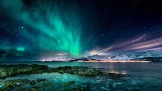 green northern lights over lake with stars