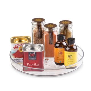 A clear plastic lazy susan with spice bottles, boxes, and essence bottles on top of it