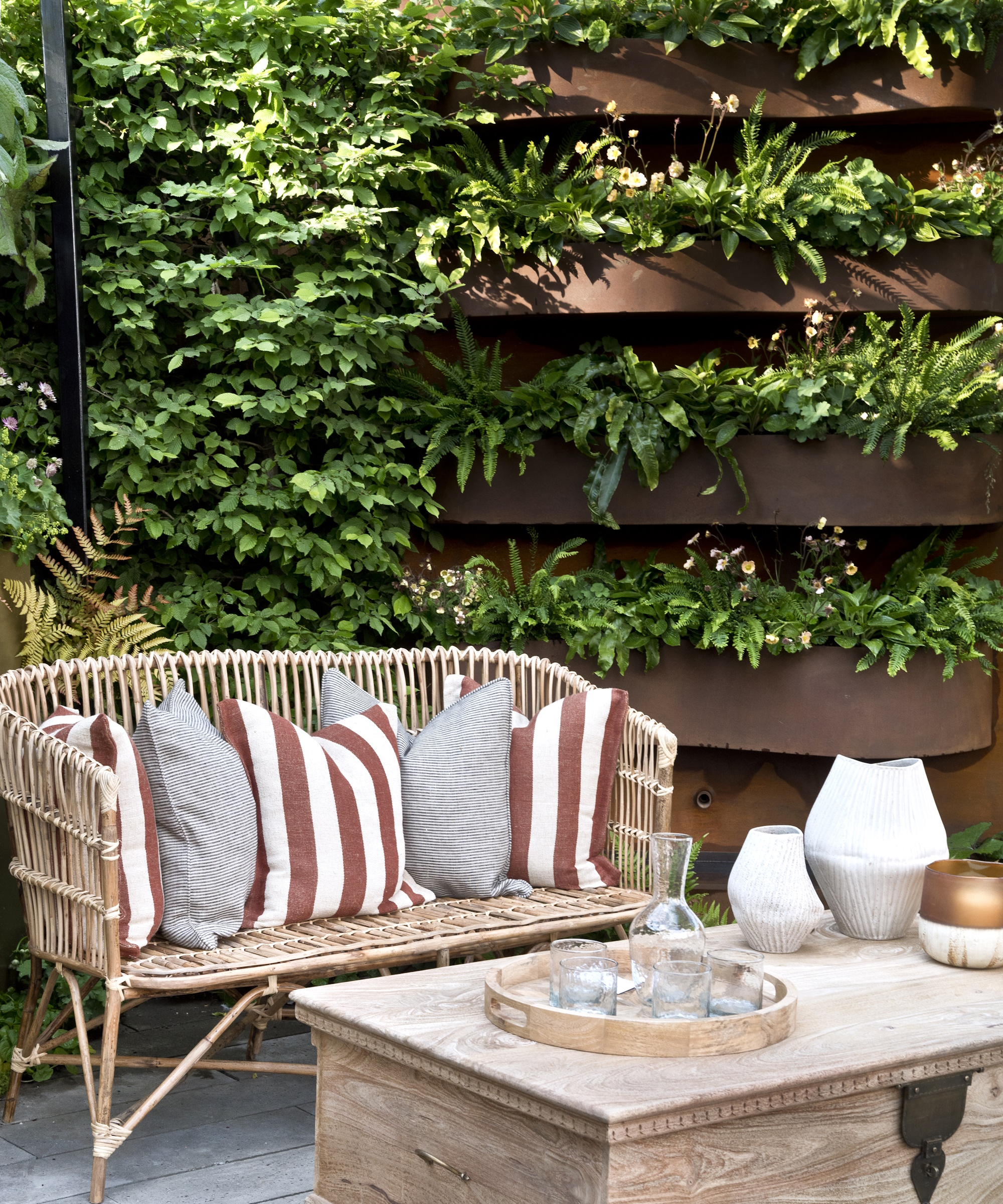 Garden sofa with brown striped cushions and wooden chest table, in front of vertical green wall