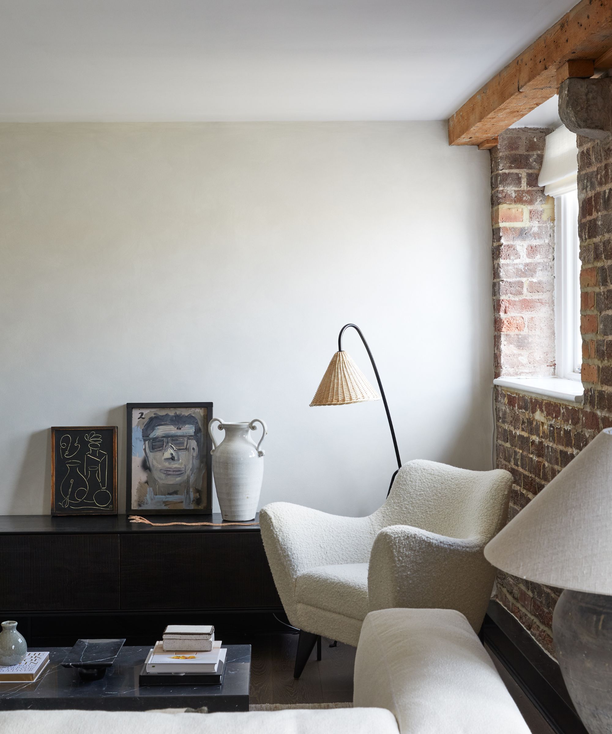 Minimalist living room with plaster walls, exposed brick walls, wooden console table with art propped up on it, floor lamp, boucle chair and whiten linen sofa