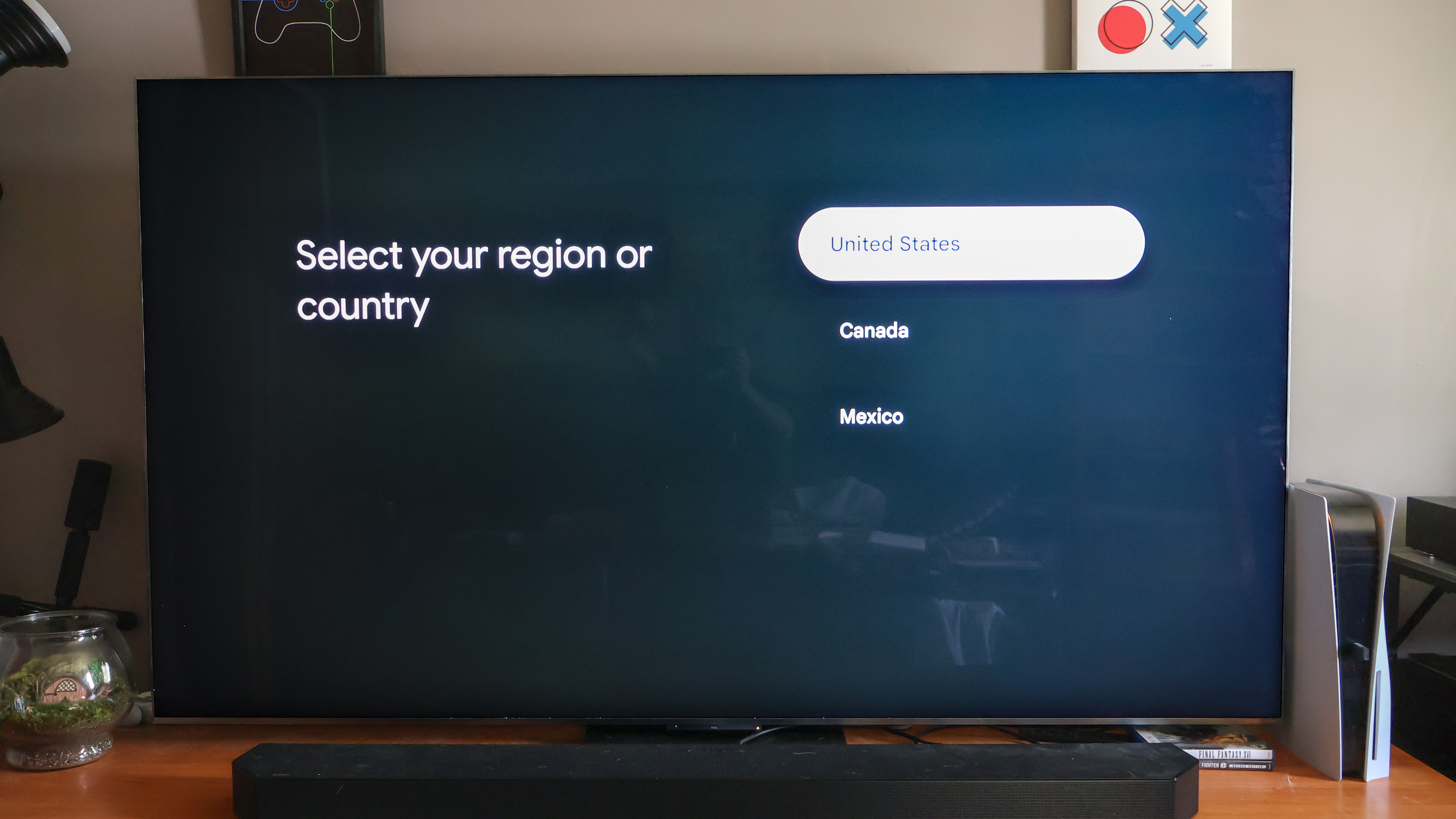 A TV on a media console displaying the step in the Google TV setup process that asks the user to select their region or country.