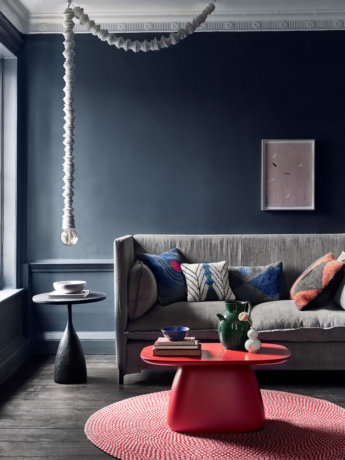 Living room with dark blue wall, grey sofa, pink rug and bold table