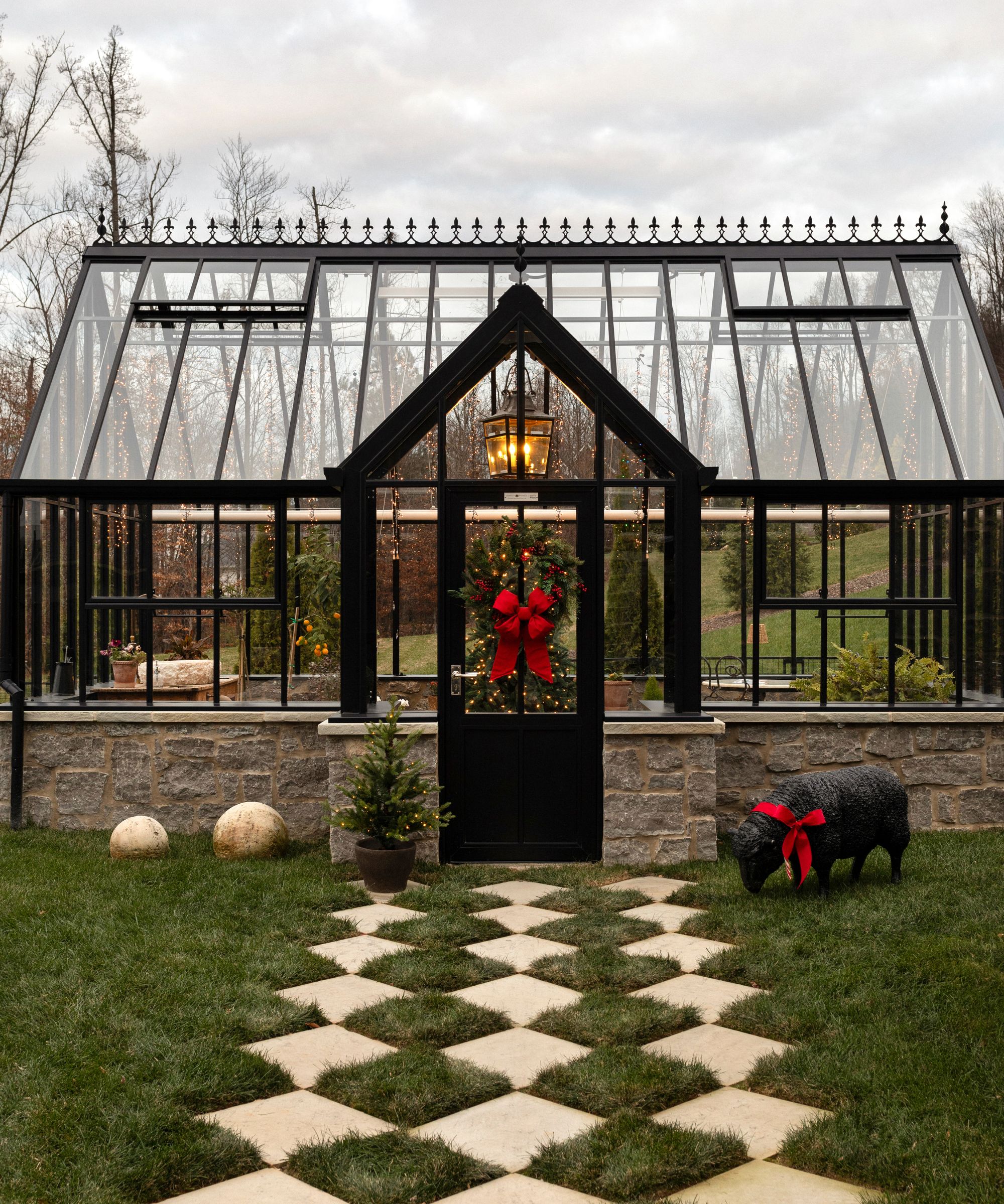 a large Victorian style glass greenhouse with a checkerboard pathway decorated for christmas with a wreath with a red ribbon