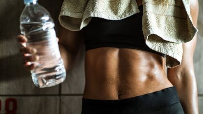 Woman with her abs exposed and holding a bottle of water