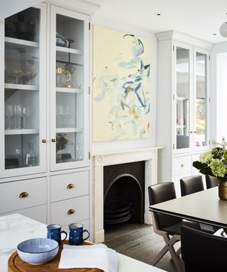 A white kitchen with a fireplace, wall artwork and glass cabinet