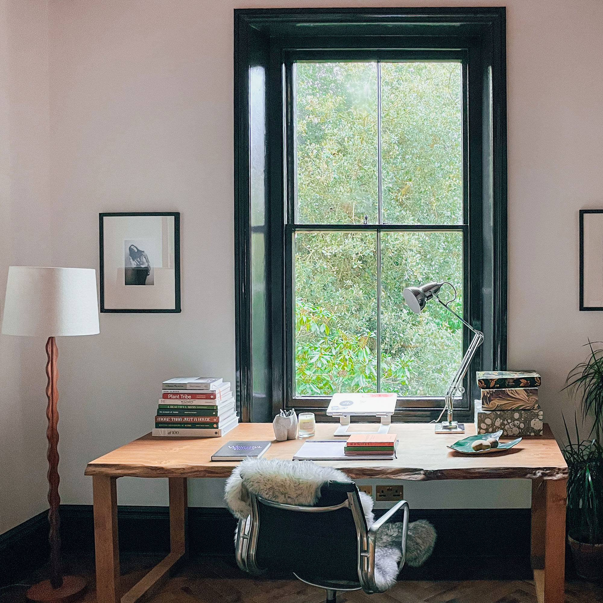Wooden desk and office chair beside wooden floor lamp in front of black-framed window