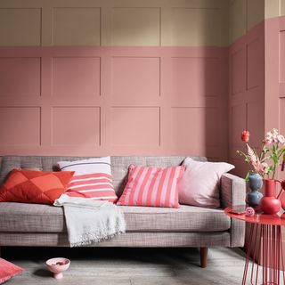 A pink living room with wall panelling and a sofa with cushions