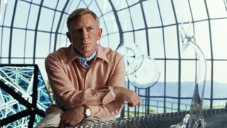 Daniel Craigs Benoit Blanc schaut jemanden aus dem Off an, während er sich in Knives Out 2 an ein Geländer lehnt.