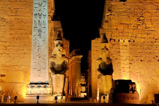 A red granite obelisk and two seated statues of Ramesses II guard the entrance to the Luxor Temple.