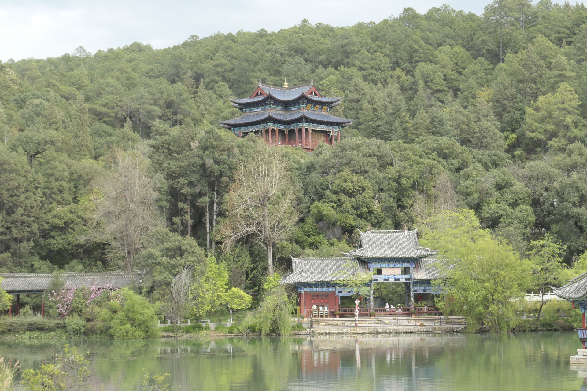 A Chinese temple nestled among trees, with a still lake in the foreground