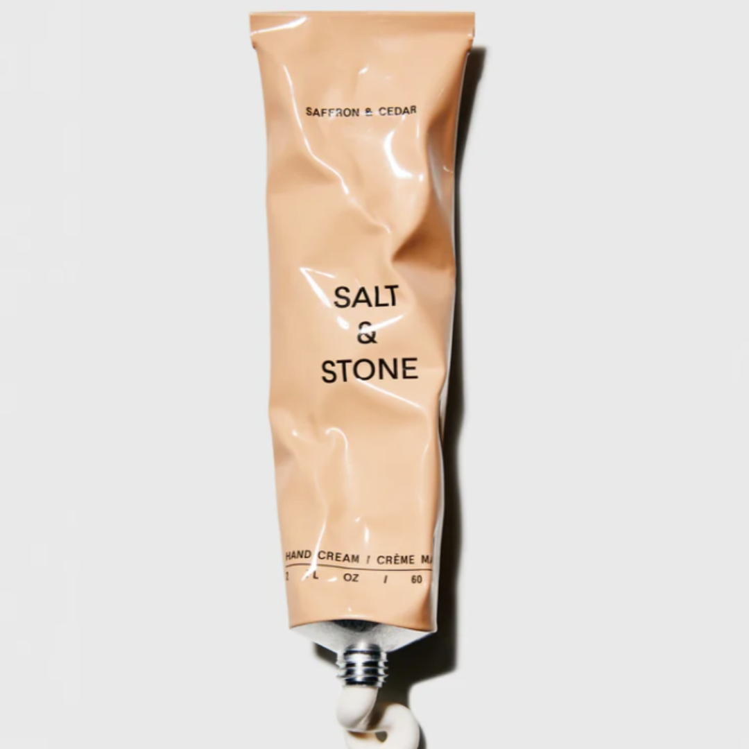 A product shot of the Salt &amp;amp; Stone hand cream in Saffron &amp;amp; Cedar: the tube has been squeeze, with some of the formula coming out onto a grey background