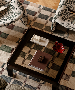 A glass-top, square coffee table sits on a geometric rug with a textured couch and patterned chairs surrounding