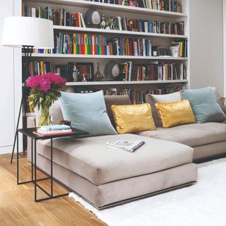 A living room with a chaise modular sofa in grey velvet and a large built-in library behind it